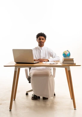 رجل سعودي بالثوب الأبيض على مكتب مع لابتوب