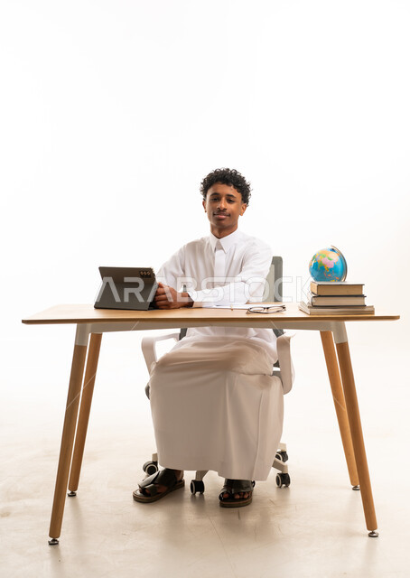 شاب سعودي بالثوب التقليدي يجلس خلف مكتب عمل