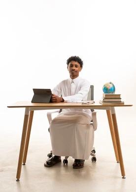شاب سعودي بالثوب التقليدي يجلس خلف مكتب عمل