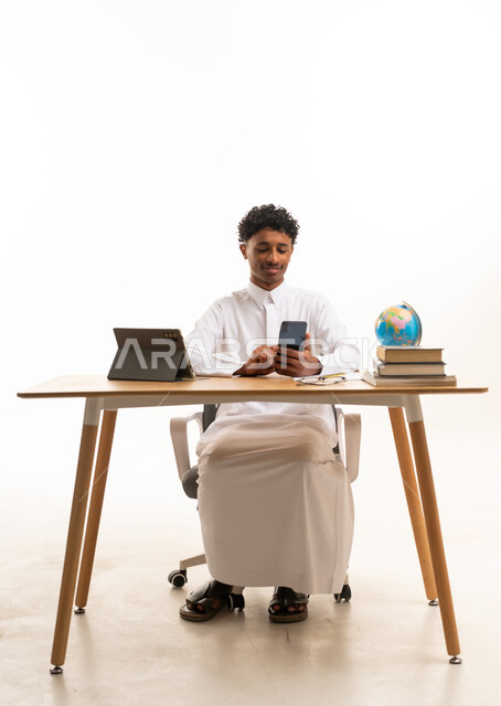 طالب سعودي بالثوب يستخدم الهاتف الذكي على المكتب