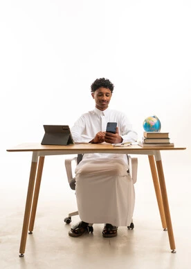Saudi Student in Thobe Using Smartphone at Desk