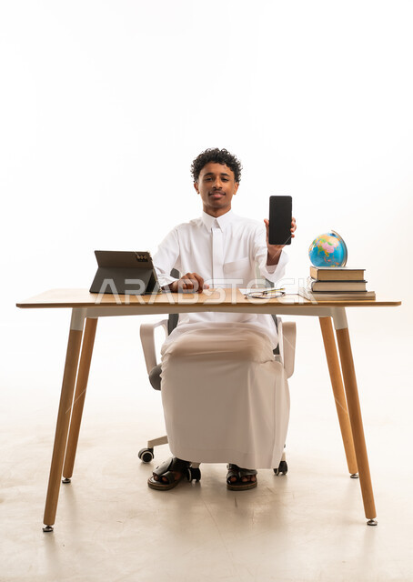رجل سعودي بالثوب يمسك هاتفاً ذكياً في المكتب