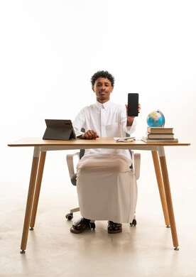 رجل سعودي بالثوب يمسك هاتفاً ذكياً في المكتب