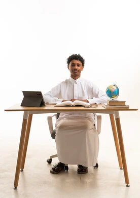 طالب سعودي بالثوب الأبيض خلف مكتب تعليمي
