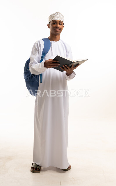 طالب عماني بالزي التقليدي يحمل كتاباً وحقيبة ظهر