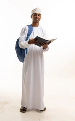 طالب عماني بالزي التقليدي يحمل كتاباً وحقيبة ظهر