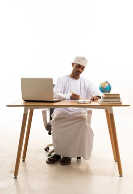 Omani Man Writing at Office Desk with Laptop