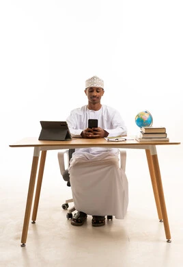 Omani Man at Desk Using Smartphone on White Background