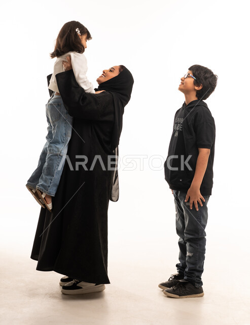 أم سعودية تحمل أطفالها أمام خلفية استوديو بيضاء ساطعة