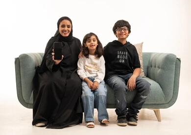 أم سعودية وأطفالها مع هاتف ذكي على الأريكة