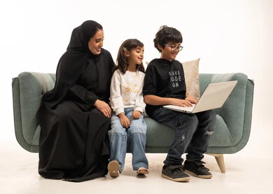 أم سعودية وأطفالها مع كمبيوتر محمول على الأريكة