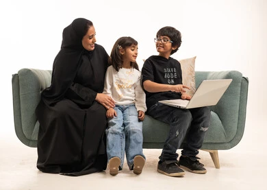 أم سعودية وأطفالها يستخدمون المحمول على الأريكة