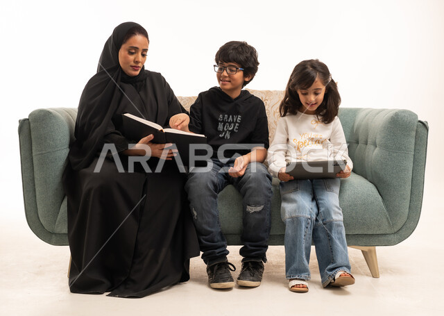 أم سعودية تقرأ مع أطفالها على أريكة زرقاء