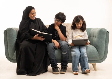 أم سعودية تقرأ كتاباً مع أطفالها على الأريكة