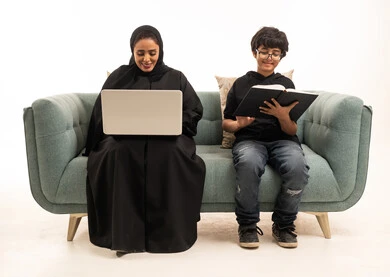 Saudi Mother and Son Learning on Sofa with Laptop and Book