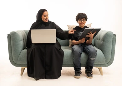أم سعودية وابنها يستخدمان الحاسوب المحمول والكتاب