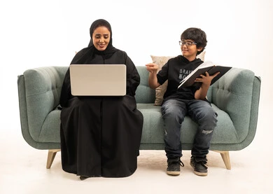 أم سعودية مع ابنها يدرسان على الأريكة باستخدام اللابتوب
