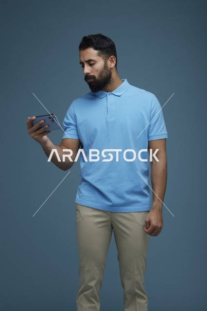 شاب سعودي يتفحص هاتف ذكي بقميص بولو أزرق