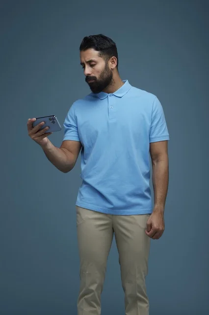 شاب سعودي يتفحص هاتف ذكي بقميص بولو أزرق