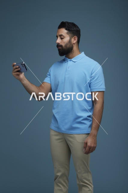 شاب سعودي يستخدم هاتف ذكي بقميص بولو أزرق في الاستوديو