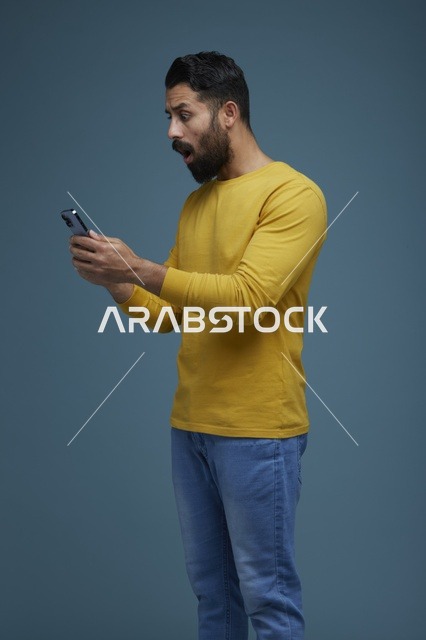 شاب سعودي مصدوم يستخدم الهاتف الذكي بملابس كاجوال