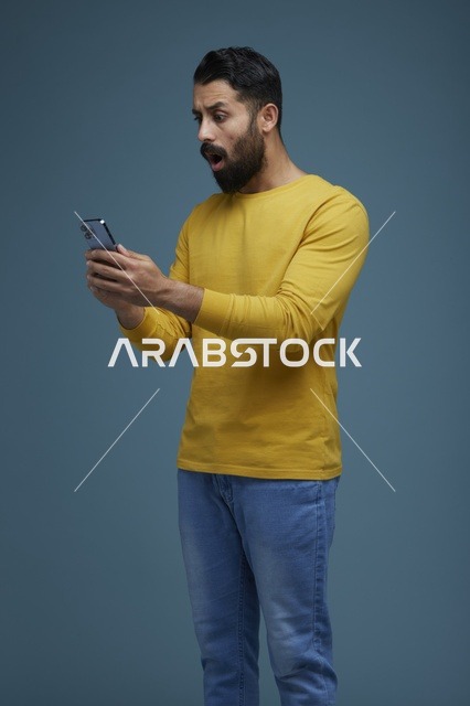 شاب سعودي مصدوم يستخدم الهاتف الذكي بملابس كاجوال