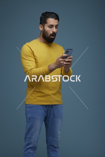 شاب سعودي مندهش يستخدم الهاتف الذكي بملابس كاجوال
