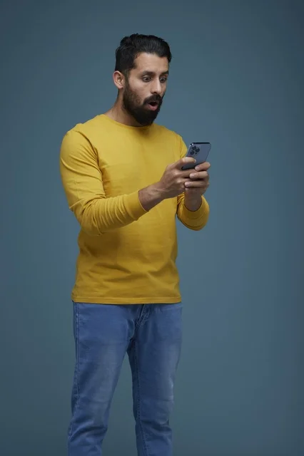 شاب سعودي مندهش يستخدم الهاتف الذكي بملابس كاجوال