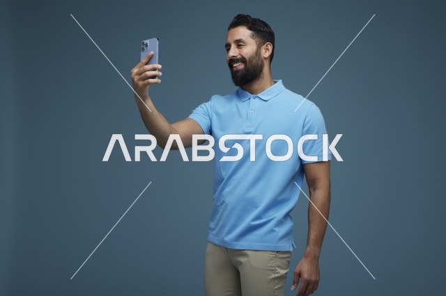 شاب سعودي يلتقط سيلفي بالهاتف بقميص بولو أزرق