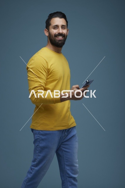 شاب سعودي يحمل هاتفاً ذكياً بخلفية استوديو