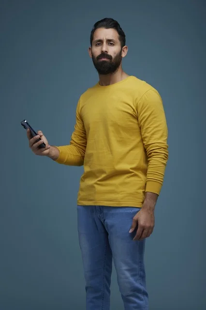 شاب سعودي يحمل هاتفاً ذكياً أمام خلفية زرقاء