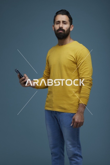 شاب سعودي يحمل هاتف ذكي بخلفية زرقاء