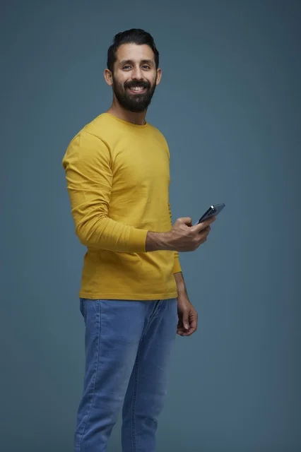 Saudi Man Holding Smartphone in Yellow Shirt Blue Background