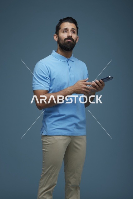 شاب سعودي يحمل هاتف ذكي وينظر للأعلى بخلفية زرقاء