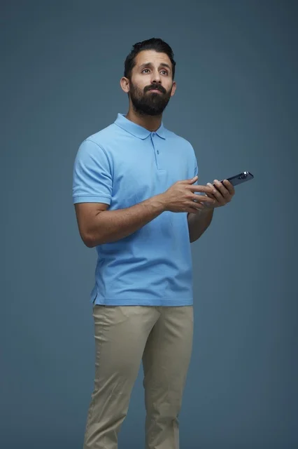 Saudi Man with Smartphone Looking Up on Blue Background
