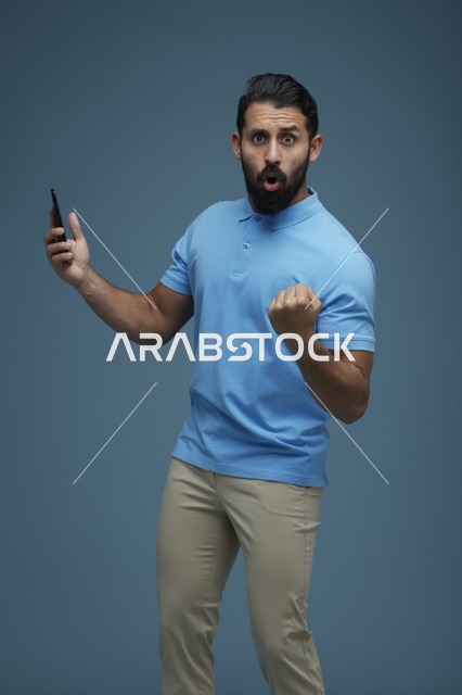 شاب سعودي يحتفل بالفوز مع هاتف ذكي على خلفية زرقاء