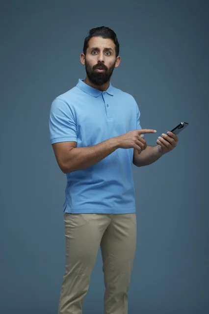 Surprised Saudi Man Pointing at Smartphone on Blue Background