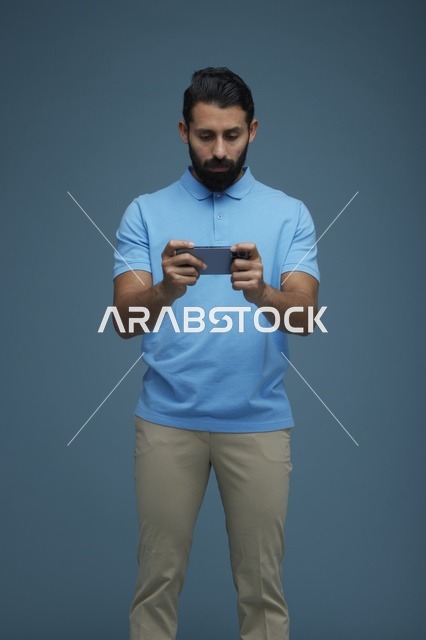شاب سعودي يلعب على الهاتف بخلفية زرقاء