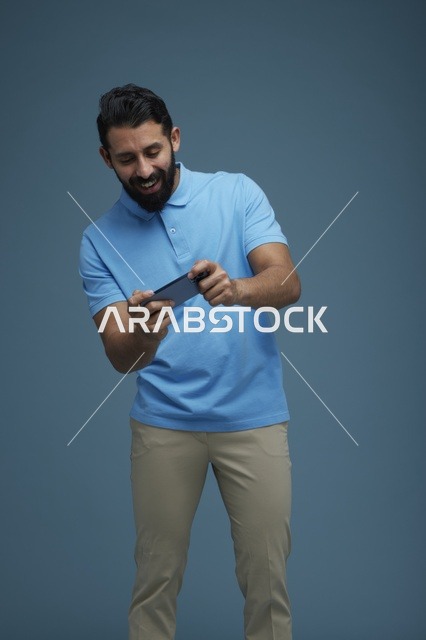 شاب سعودي يلعب على الجوال بملابس كاجوال زرقاء