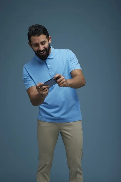 Saudi Man Playing Mobile Game in Casual Blue Polo