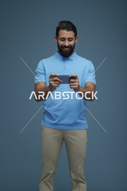 شاب سعودي يلعب لعبة على الهاتف بخلفية زرقاء