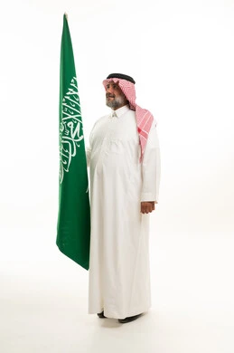 رجل سعودي بالزي التقليدي يحمل علم المملكة العربية السعودية