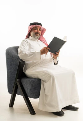 Middle-aged Saudi Man Reading Book in White Thobe