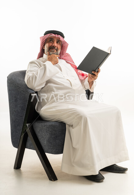 رجل سعودي بالزي التقليدي يقرأ كتاباً في استوديو