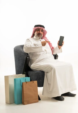 رجل سعودي مع هاتف ذكي وحقائب تسوق