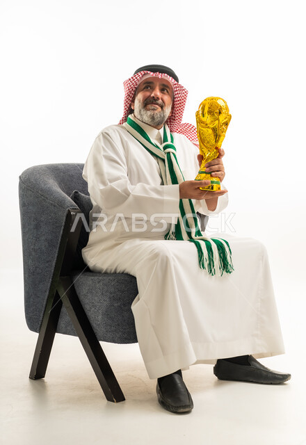 رجل سعودي يحمل كأساً ذهبياً يجلس على كرسي في الاستوديو