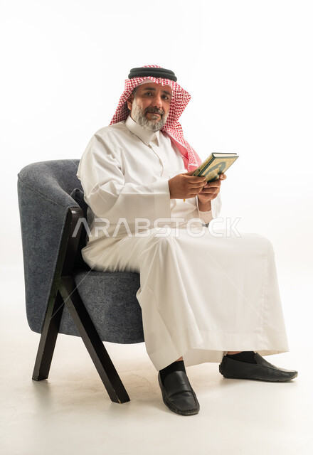 رجل سعودي بالثوب التقليدي يجلس ممسكاً بكتاب