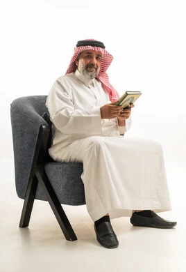 رجل سعودي بالثوب التقليدي يجلس ممسكاً بكتاب