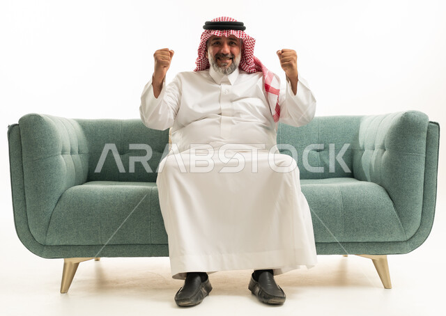 رجل سعودي بالثوب التقليدي يحتفل على الأريكة