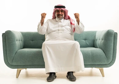 Saudi Man in Traditional Thobe Celebrating on Sofa